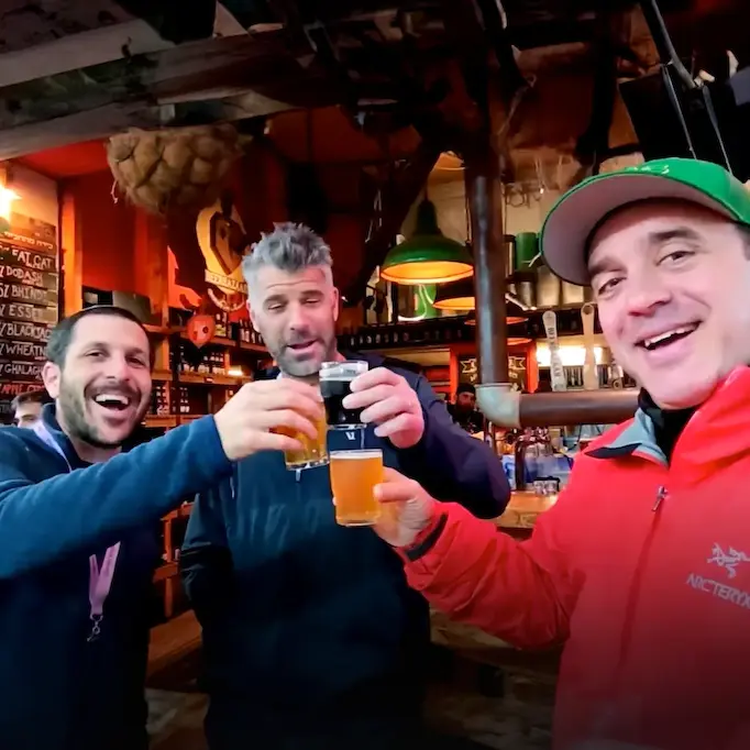 Group of men standing at a bar entrance, raising their beers in a toast, smiling and enjoying their time
