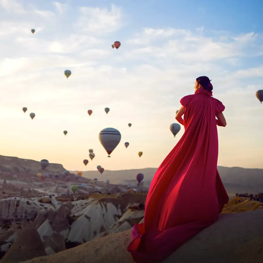 Woman in a flowing red dress watching hot air balloons in Cappadocia, Turkey.