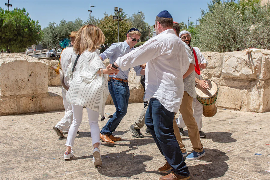 Family and musicians dancing together in celebration near ancient Jerusalem stone walls.