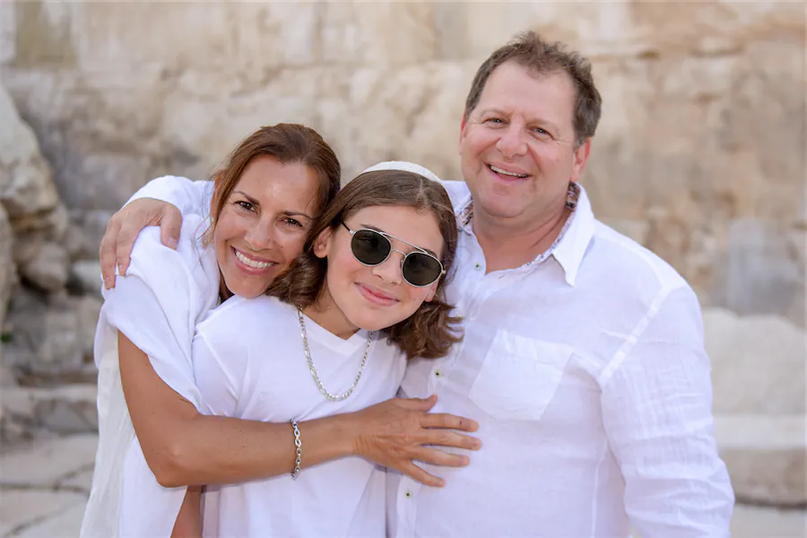 A Bar Mitzvah boy shares a warm hug with his smiling parents at a historic Jerusalem site.