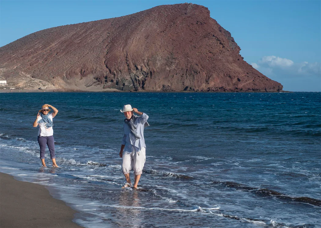 A couple enjoying a beach walk with volcanic mountains in the Canary Islands, Spain, offering warm temperatures and a subtropical climate year-round.